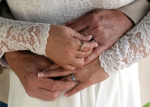 Close-up of hands with wedding rings against white lace dress fabric.