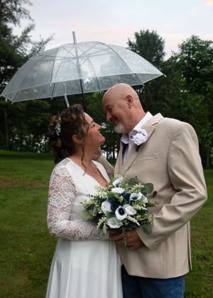 Wedding couple sharing intimate moment under clear umbrella in garden setting.