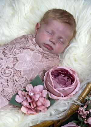 Sleeping baby in pink lace wrap with roses on white fur background.