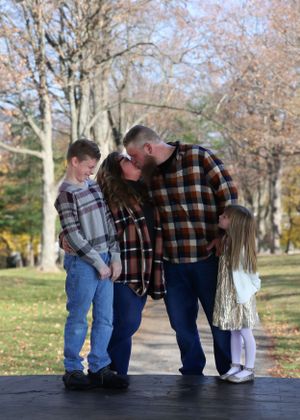 An autumn outdoor family photo with matching plaid shirts on a pathway surrounded by fall foliage.