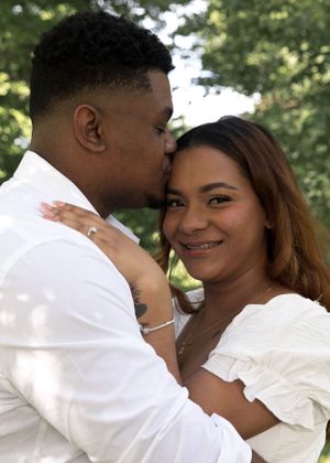 A romantic couple in white outfits sharing an intimate moment outdoors with trees in the background.