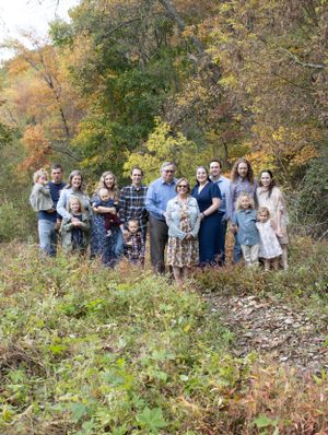 Large family group poses together outdoors during autumn with colorful fall foliage in background.