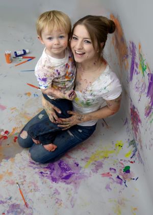 Messy paint play session with colorful splatters on wall and floor.