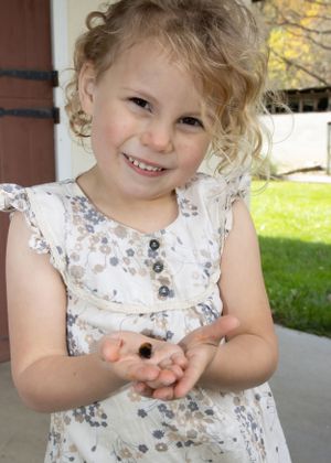 A young child in a floral dress smiles while playing outdoors on a sunny day.