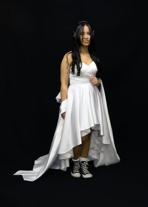 A dramatic portrait with a white high-low dress and sneakers against a black background.