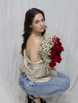 Artistic portrait holding red roses and baby's breath bouquet while wearing casual denim and sweater.