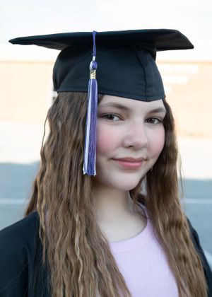 Graduate wearing black cap with blue tassel poses in traditional graduation attire.