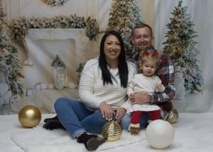 A holiday family portrait in front of decorated Christmas trees with festive ornaments and winter decor.