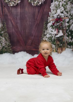 A festive holiday photo setup with red outfit against a rustic wooden door backdrop with snow and greenery decorations.