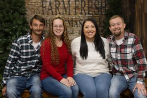 Group of four people in casual plaid and sweaters posing by rustic farm fresh sign.