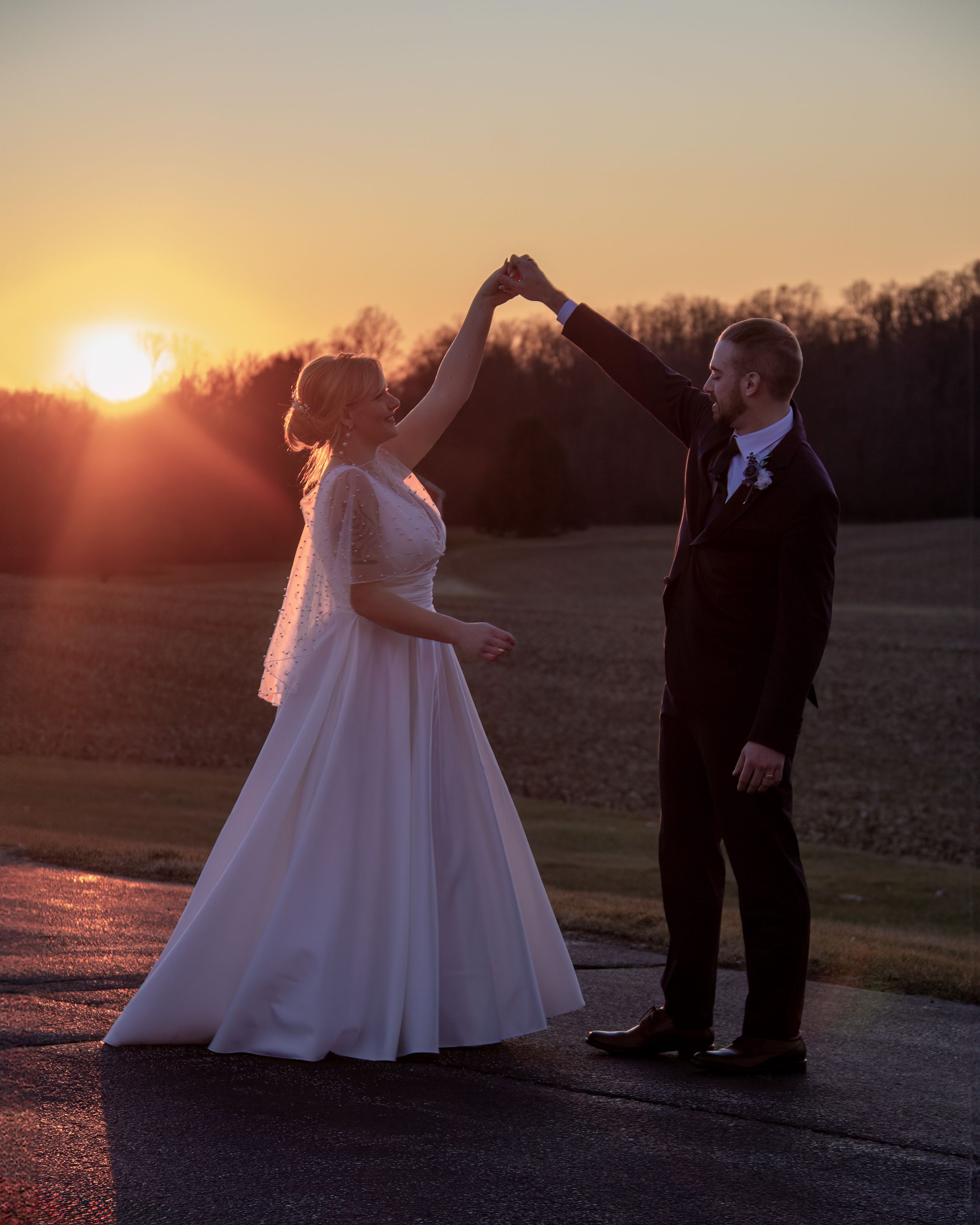 Romantic sunset dance photo of couple in wedding attire spinning in golden light.