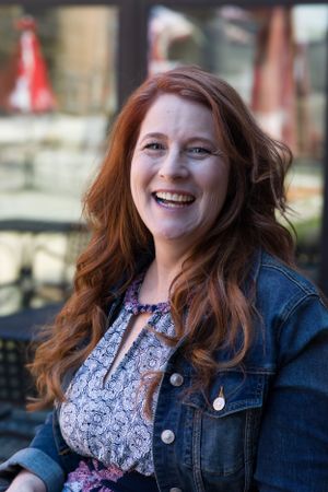 Portrait of someone wearing a denim jacket and patterned top against an outdoor background.