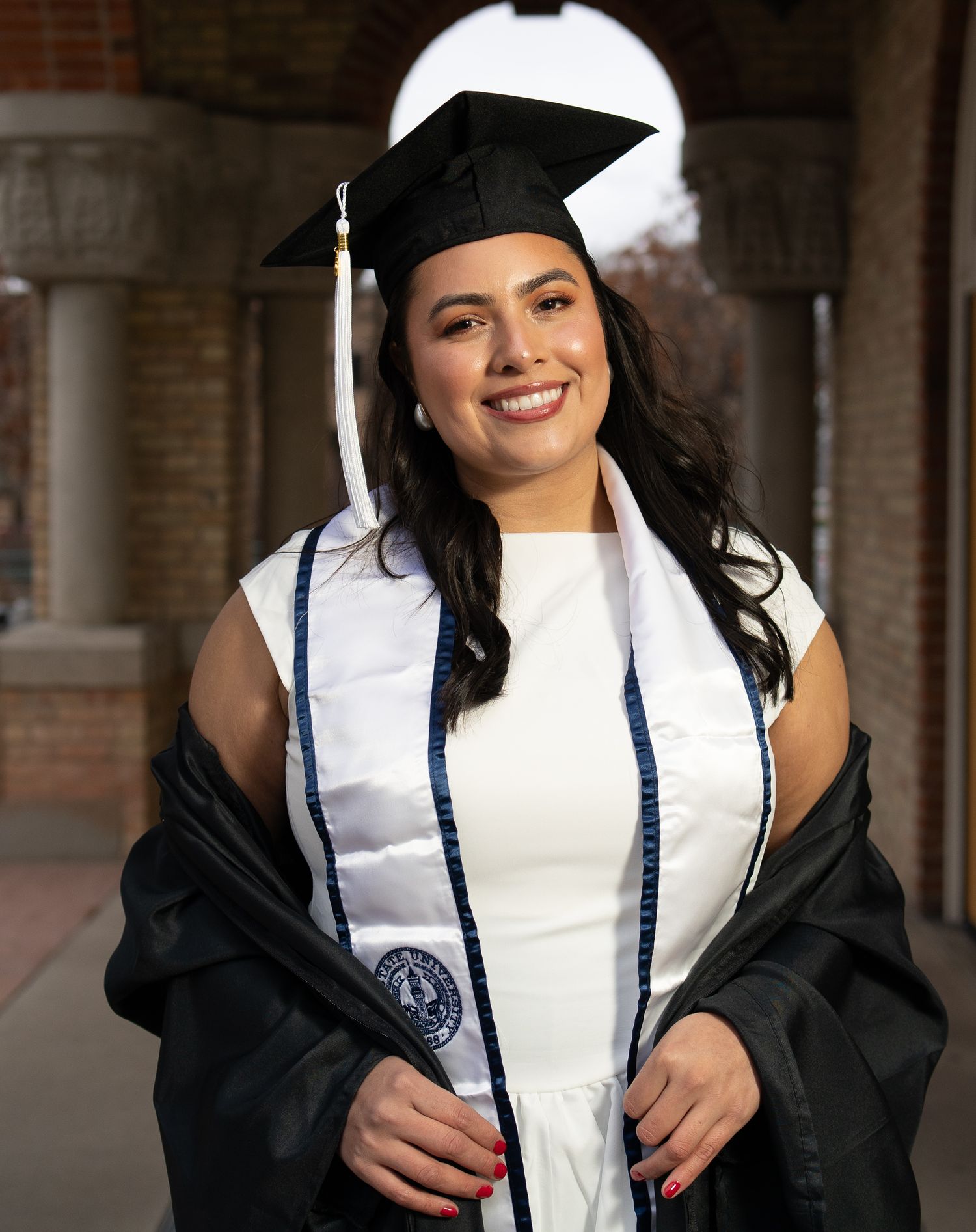 A woman wearing USU cap and gown smiling for her portrait for a graduation session in Logan, UT during golden hour.
