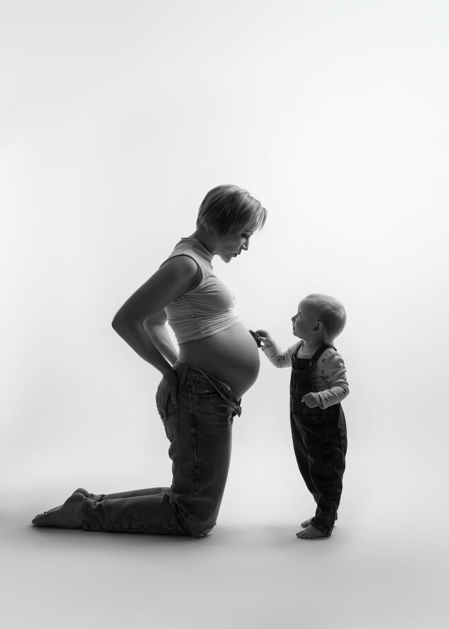 maternity photo shoot in studio with a toddler driving a small car over their mama's baby bump