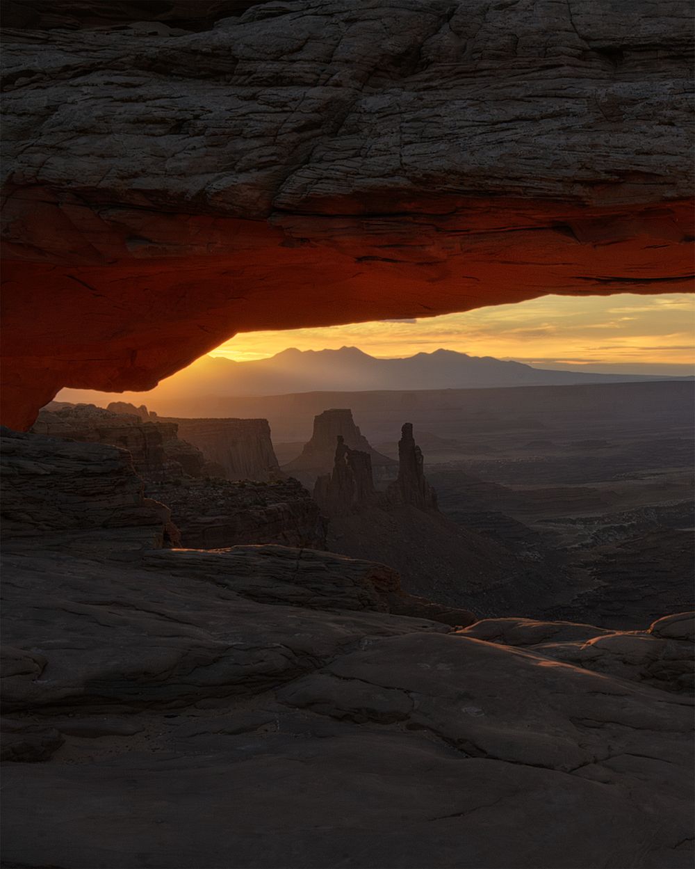 Mesa Arch in Canyonlands National Park frames a dramatic sunset view over desert rock formations in Utah.