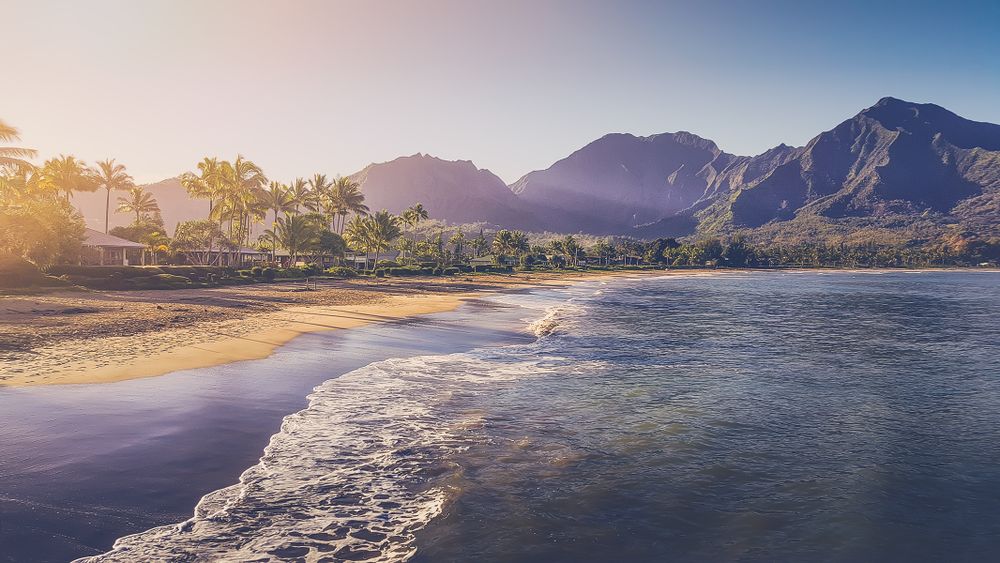 Gentle waves roll onto Hanalei Bay beach at sunrise with majestic Na Pali mountains in background, Kauai, Hawaii.