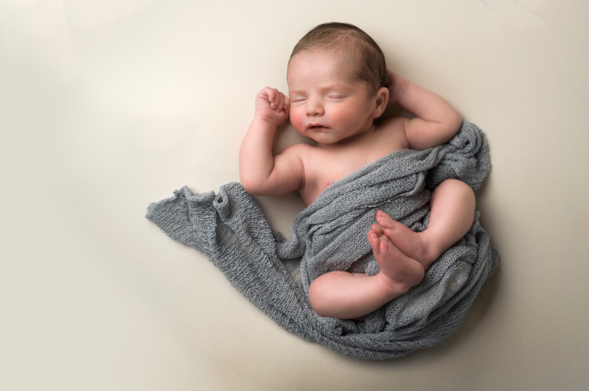 Peaceful newborn baby wrapped in a soft gray knit blanket, sleeping curled up on a cream background. Embracing Life’s Beauty