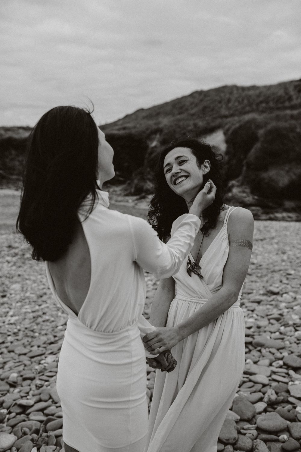 Black and white photo of two people sharing tender moment on rocky beach.