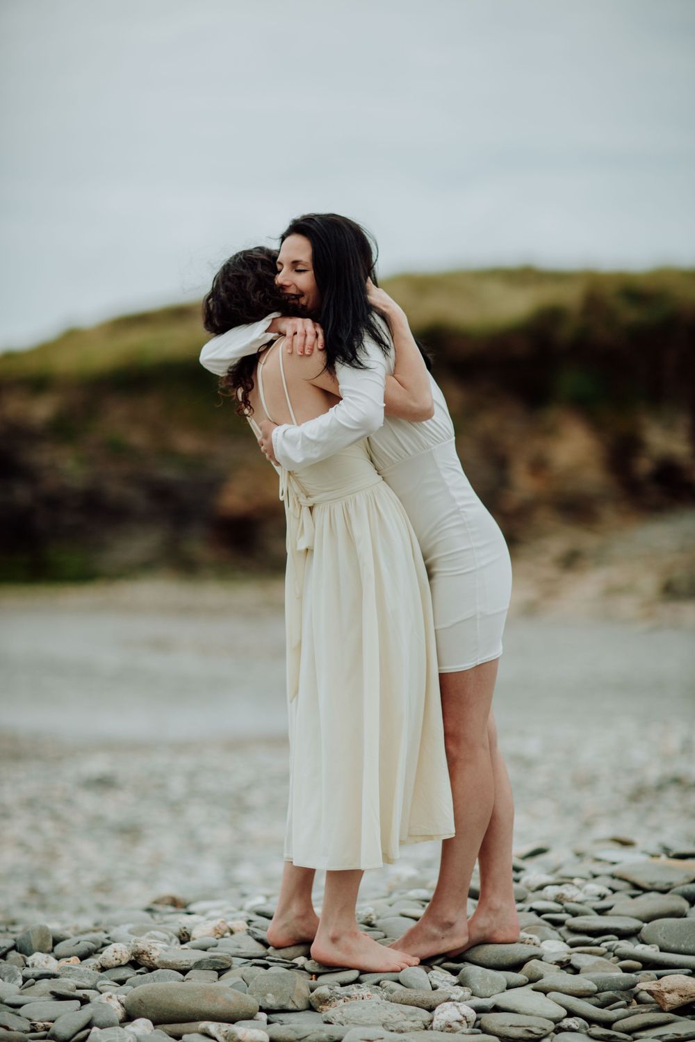Loving embrace shared between two people in white dresses on rocky coastline.