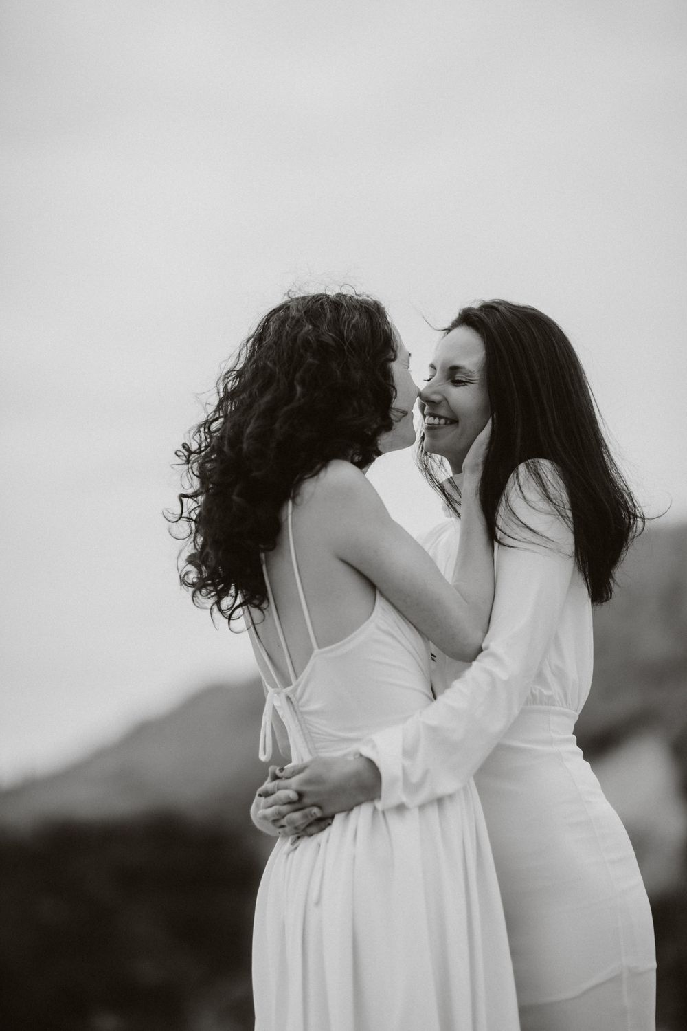 Black and white portrait of a couple in white dresses embracing outdoors.