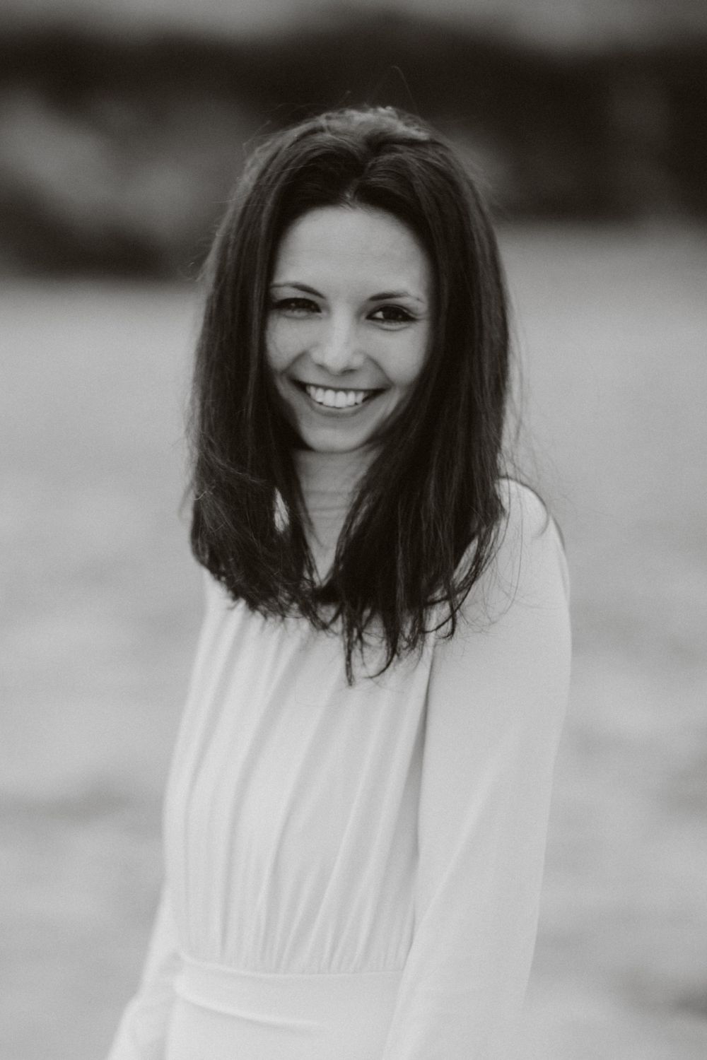 Black and white portrait of a person in white dress with dark hair smiling warmly.