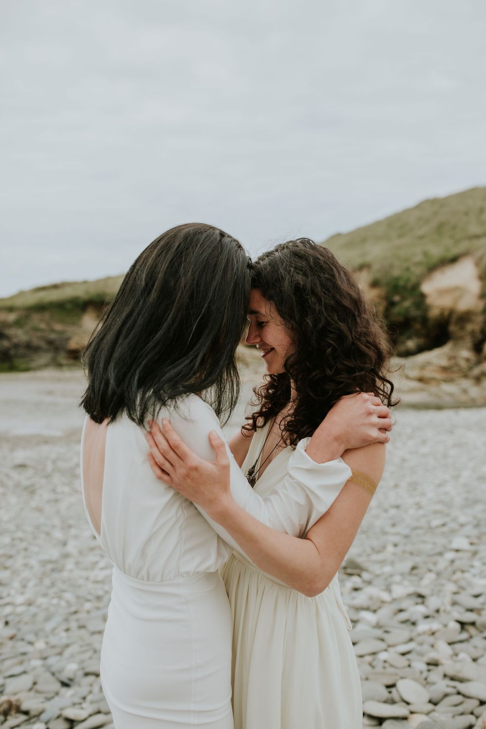 Intimate moment between two people in white dresses on rocky beach.
