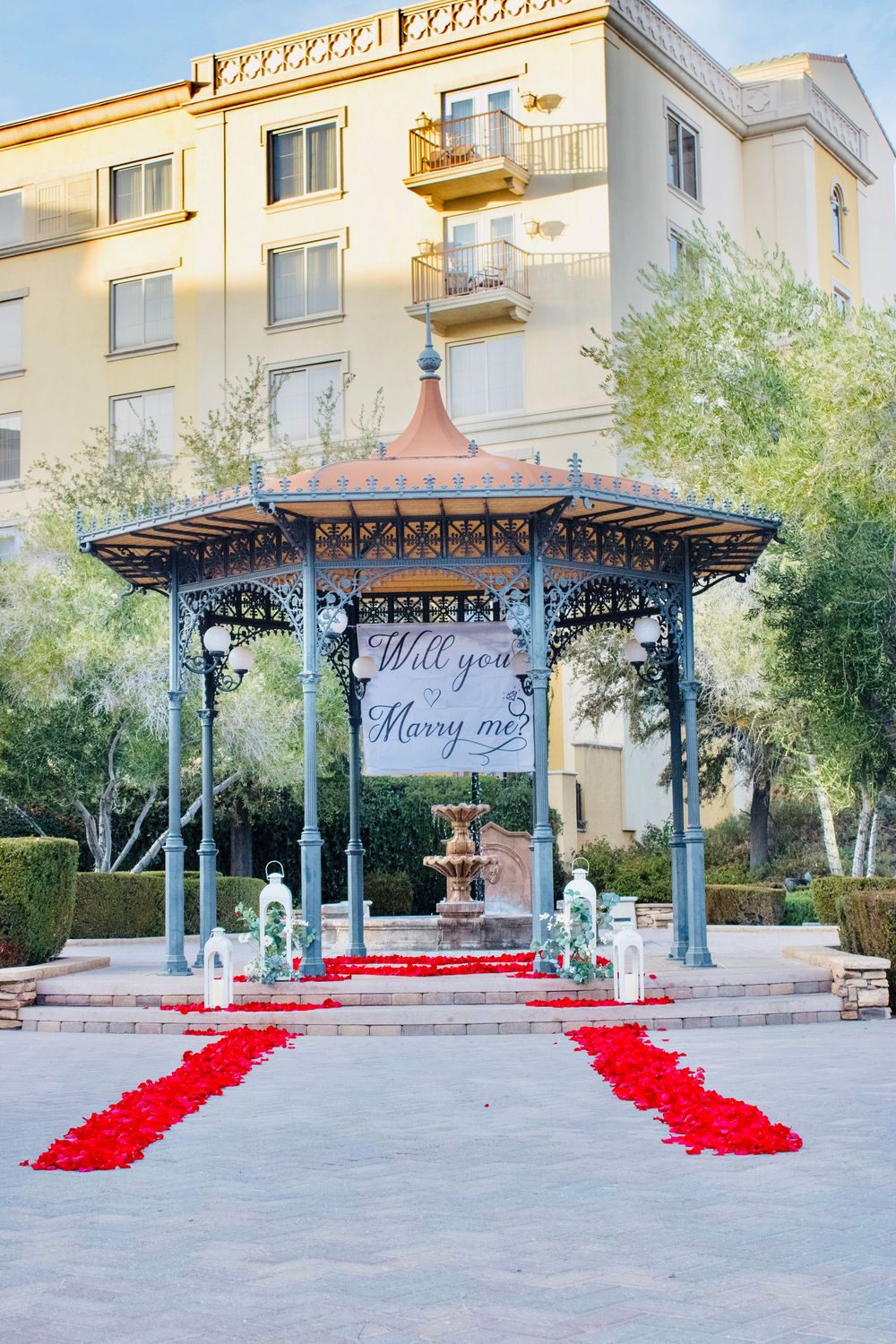 Elegant gazebo proposal setup with red rose petal path and Will You Marry Me banner.