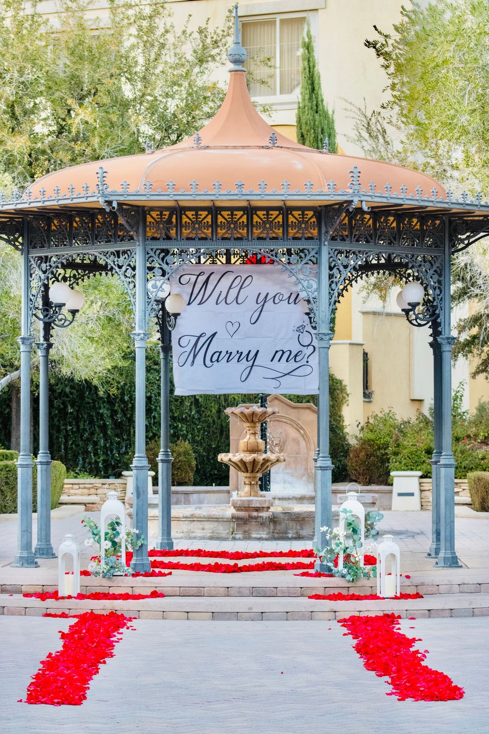 Elegant gazebo decorated with red rose petals and a Will You Marry Me banner for a proposal.
