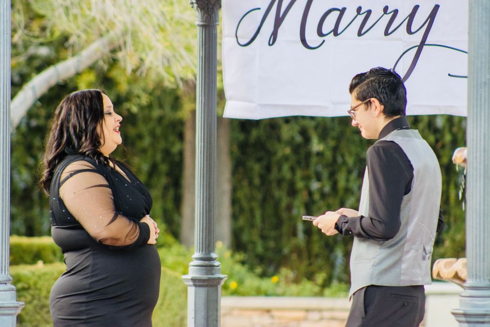 A couple shares a romantic moment under a Will You Marry Me banner during an outdoor marriage proposal.