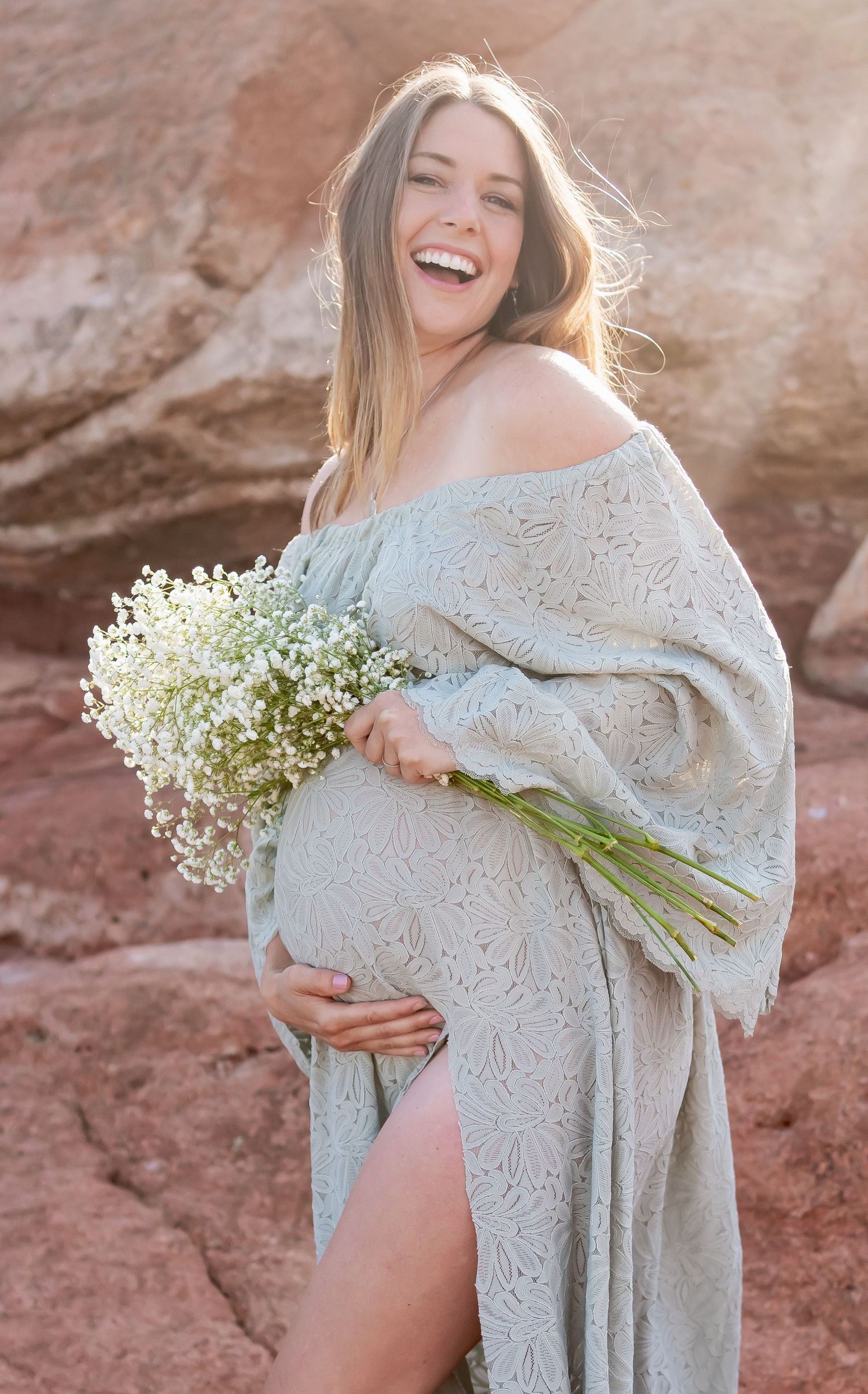 Joyful maternity moment captured with baby's breath bouquet against red rock backdrop.