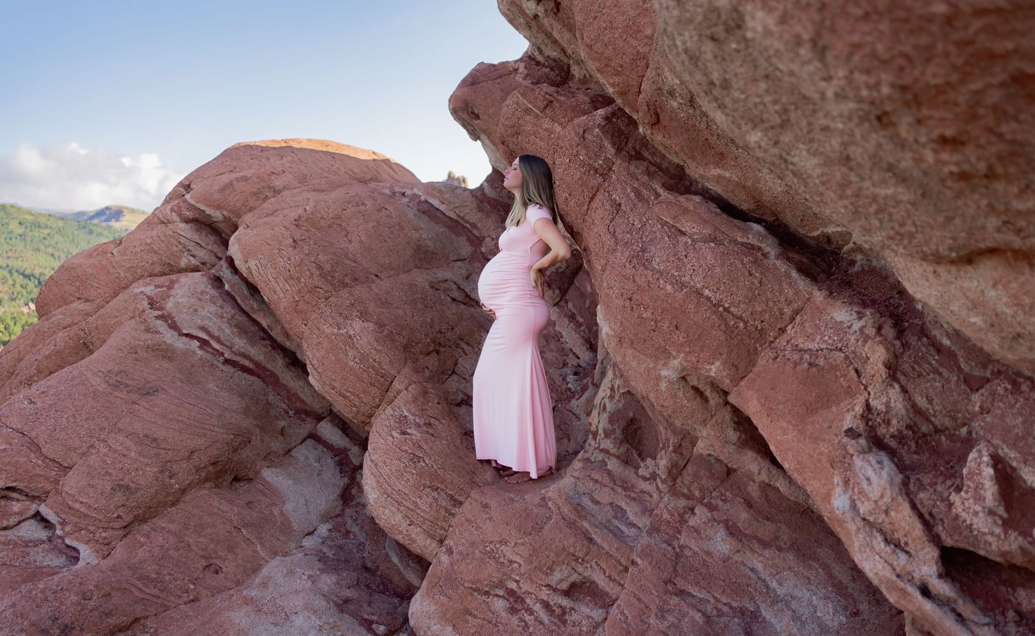 A maternity photo shoot featuring a flowing pink dress against dramatic red rock formations.