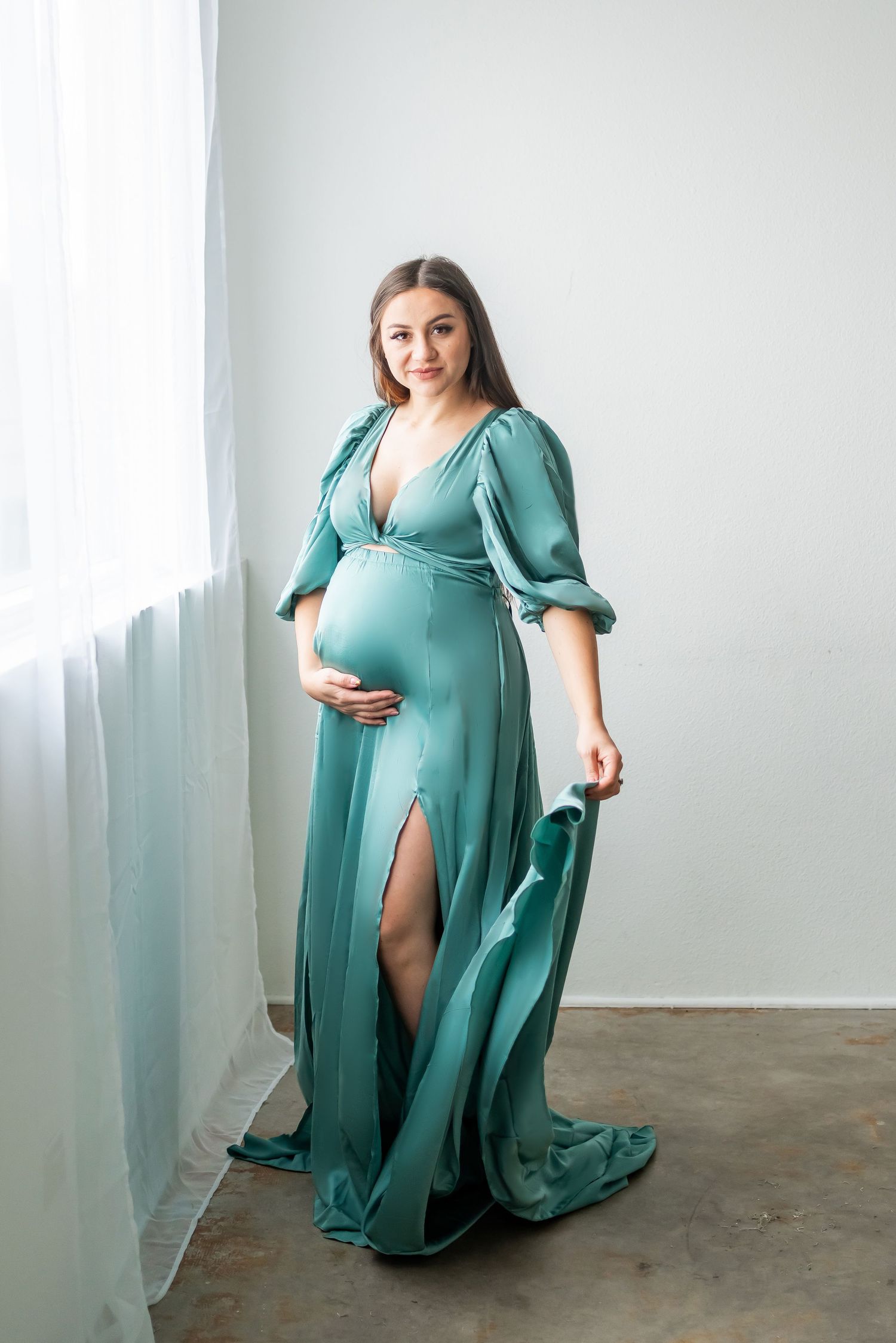 Stunning teal maternity dress with puffy sleeves and high slit in bright studio setting.