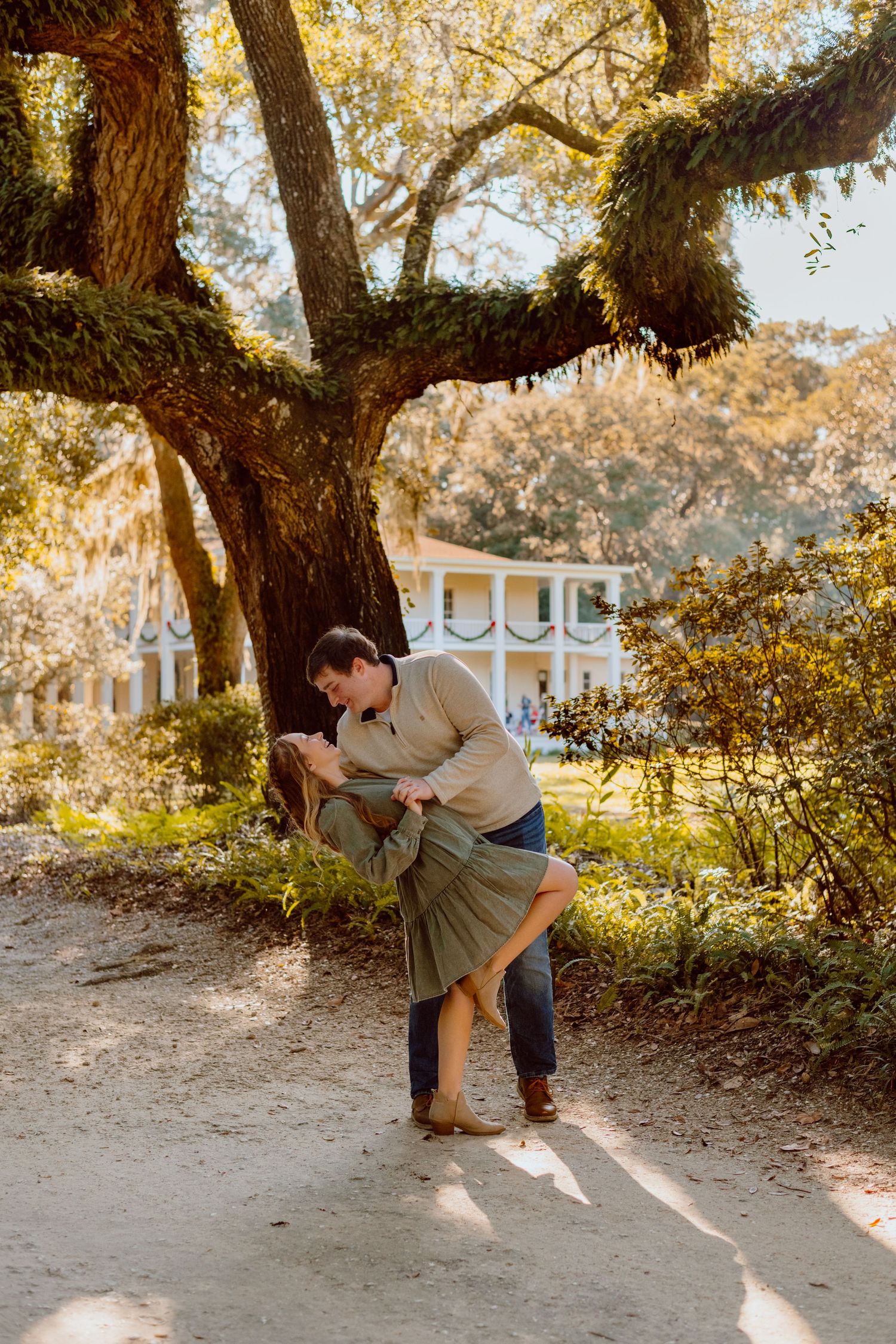 Romantic couple sharing intimate moment under moss-covered tree at sunset.
