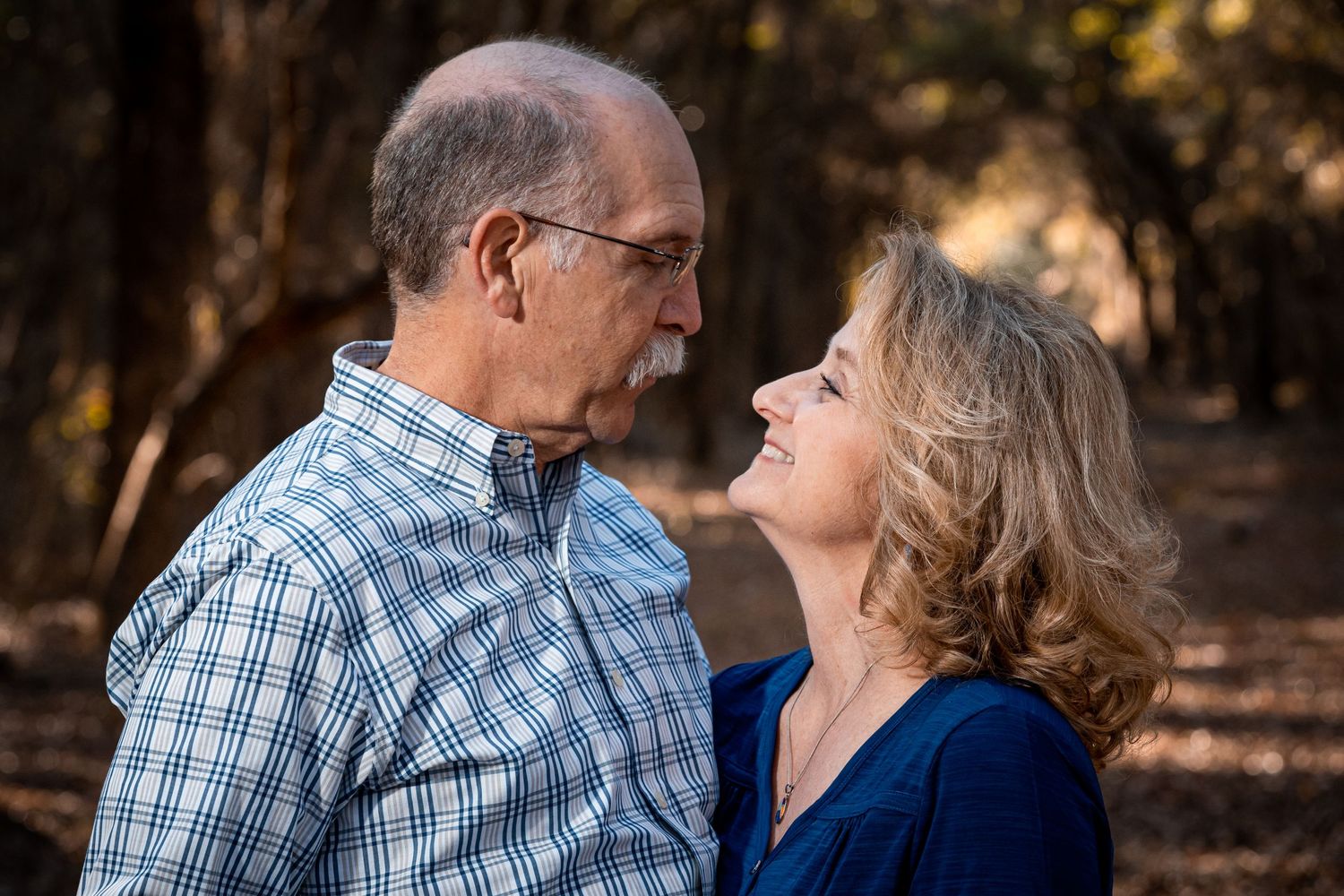 A mature couple sharing an intimate moment in a wooded setting.