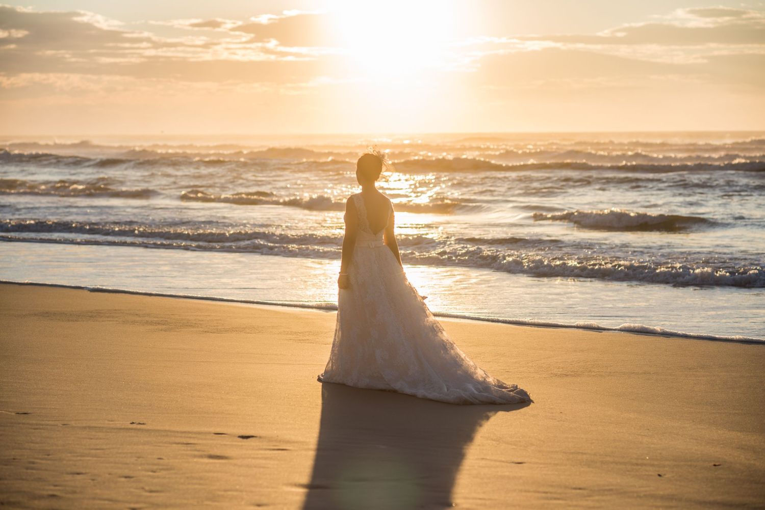 Silhouette of flowing wedding dress against dramatic ocean sunset.