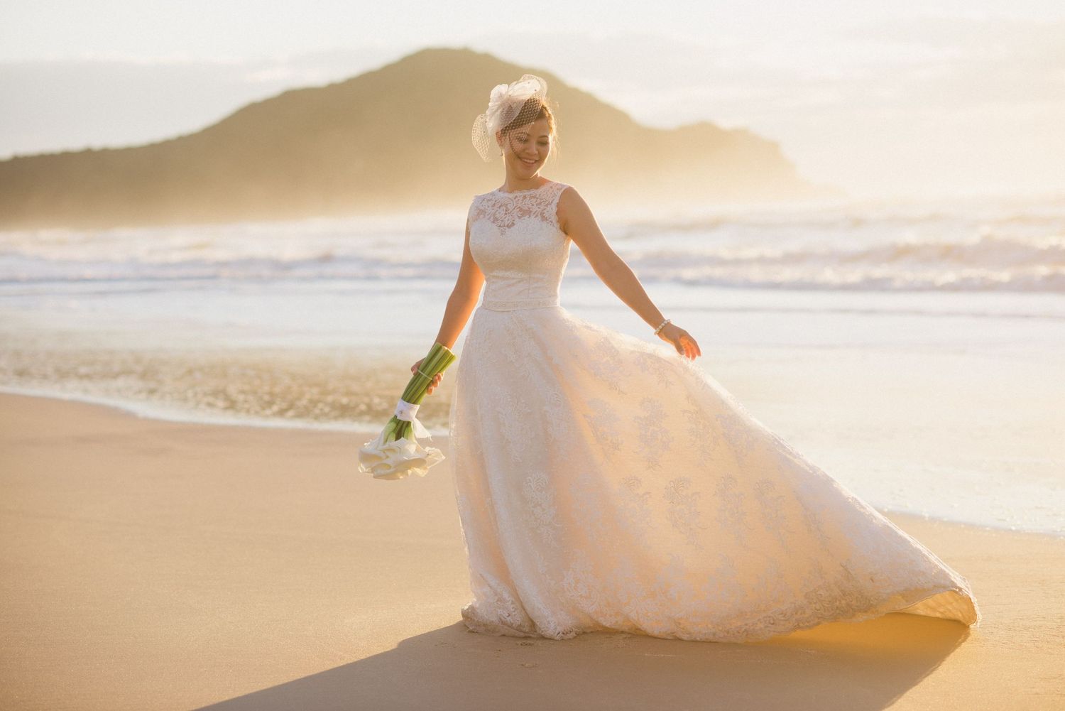 Beautiful beach bridal portrait with flowing dress and mountain backdrop at golden hour.