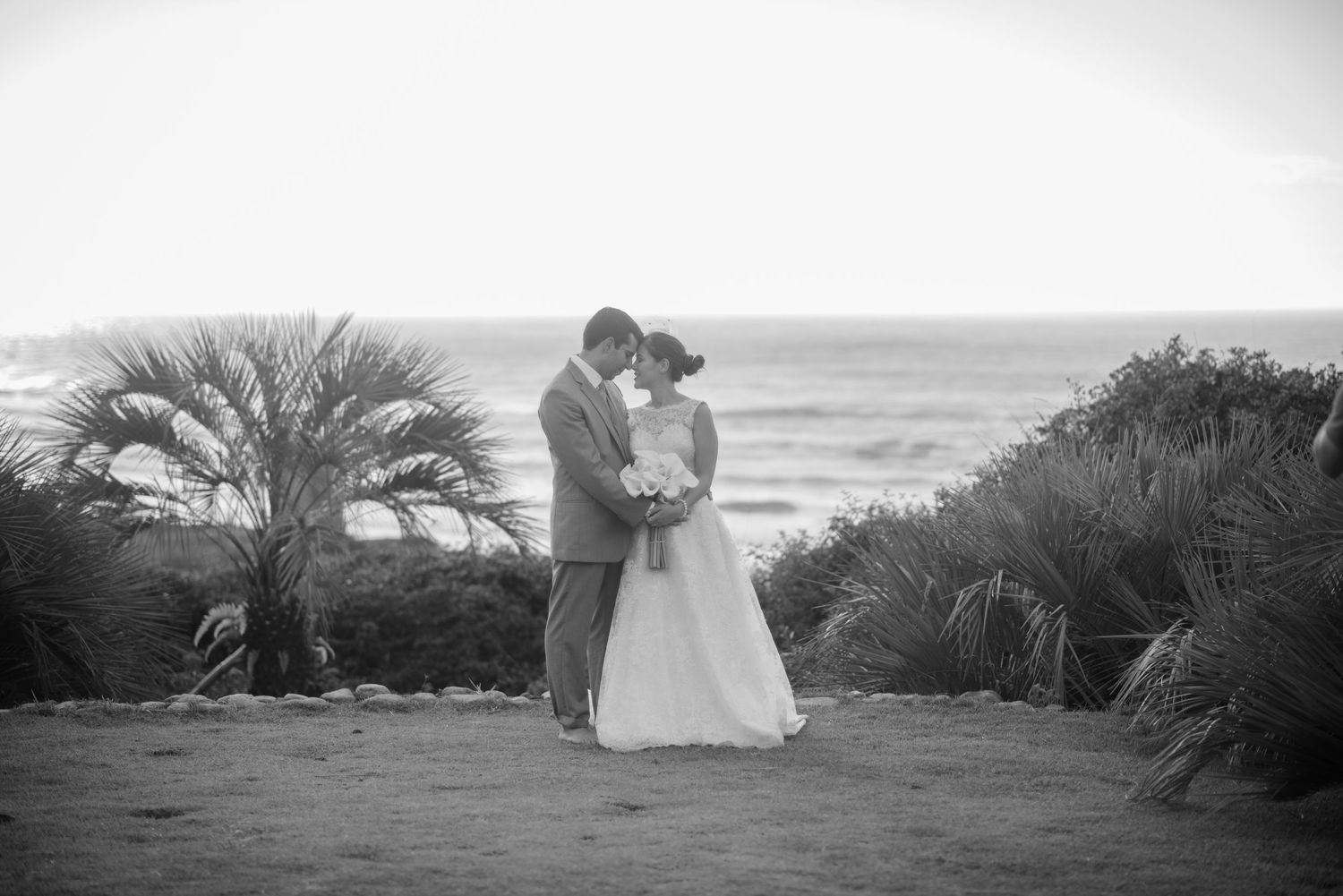 Black and white romantic beach portrait with coastal vegetation and ocean backdrop.