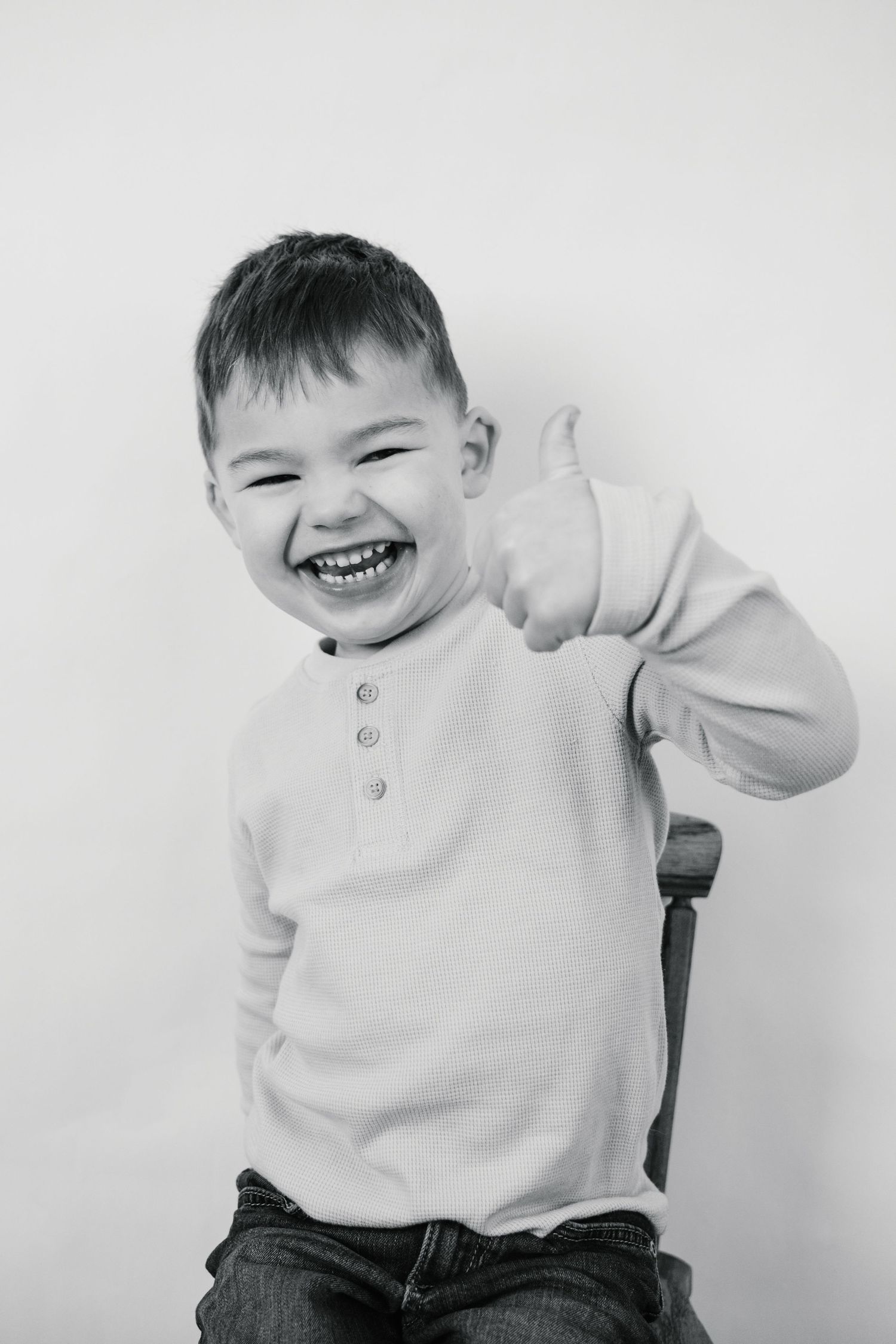 Happy young boy giving a thumbs up and laughing in a black and white studio portrait.