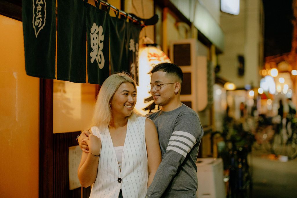 Couple exploring traditional Japanese alleyway decorated with lanterns and noren curtains.
