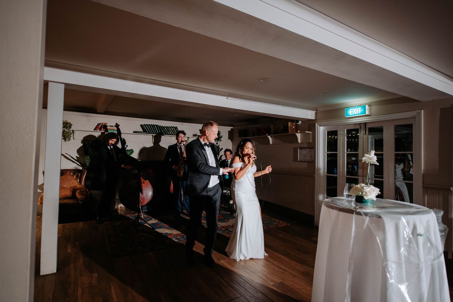 Wedding guests dancing and celebrating on a wooden dance floor at an indoor reception venue.