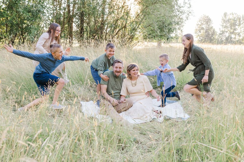 Happy family of seven sits and plays together in a lush green meadow during golden hour.