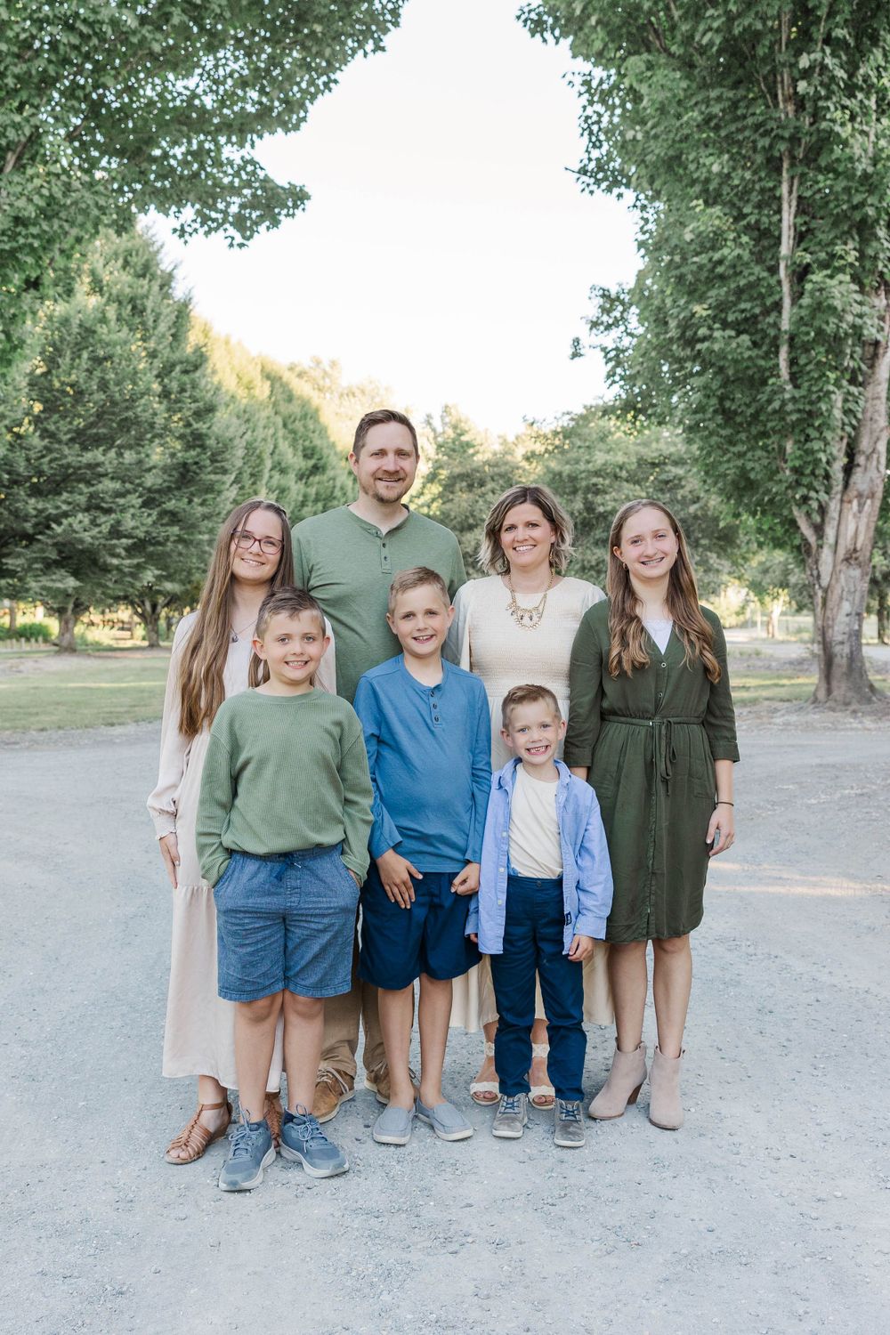 Family of seven smiles together on a tree-lined path during a warm summer evening.