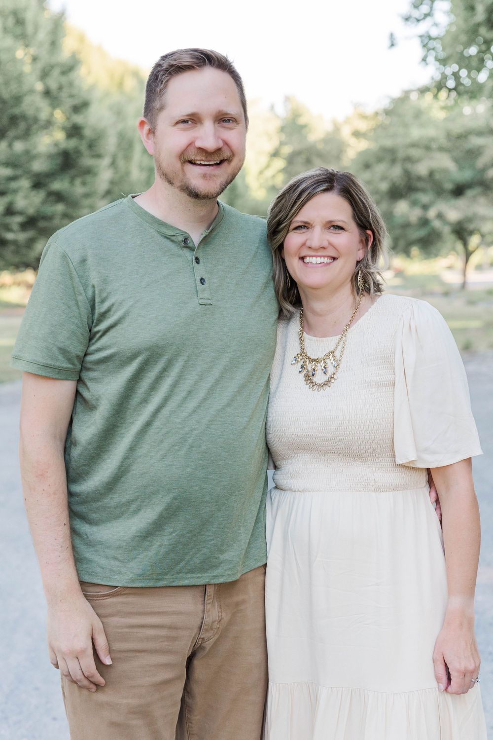 Smiling couple poses together on a tree-lined path during a warm summer family session.
