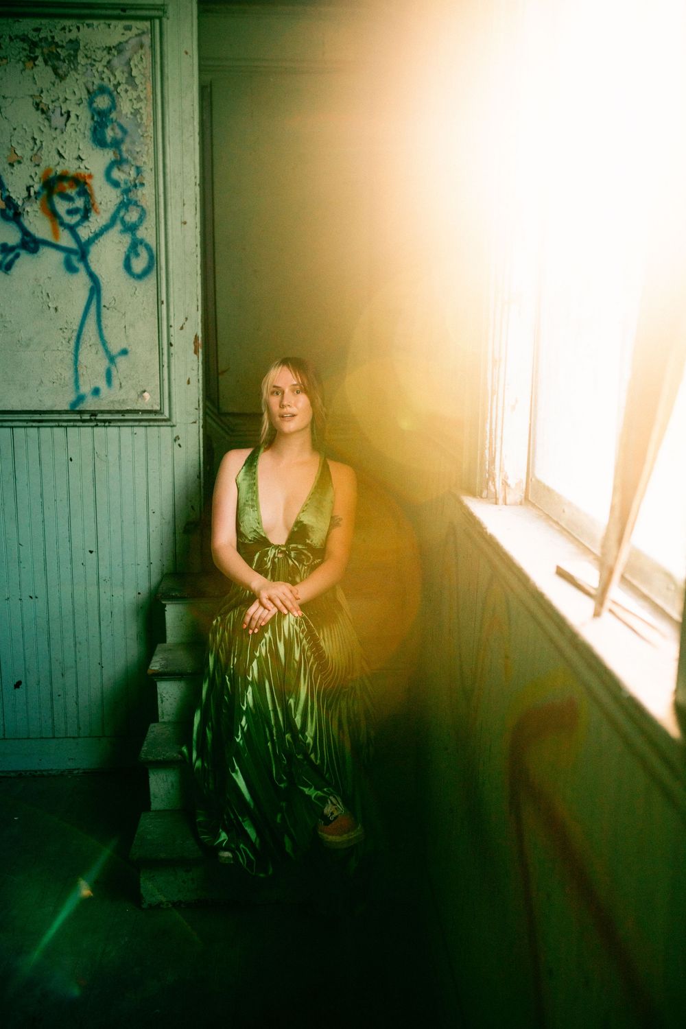 Sunlit interior scene featuring a person in black dress sitting by a bright window with ethereal golden light streaming in.