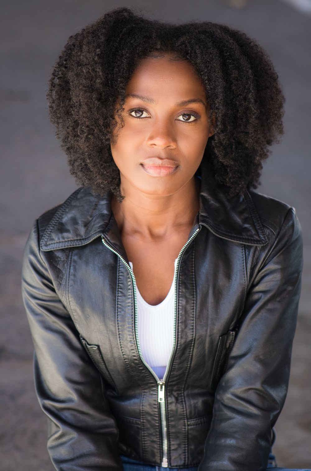 Professional portrait in leather jacket against neutral background.