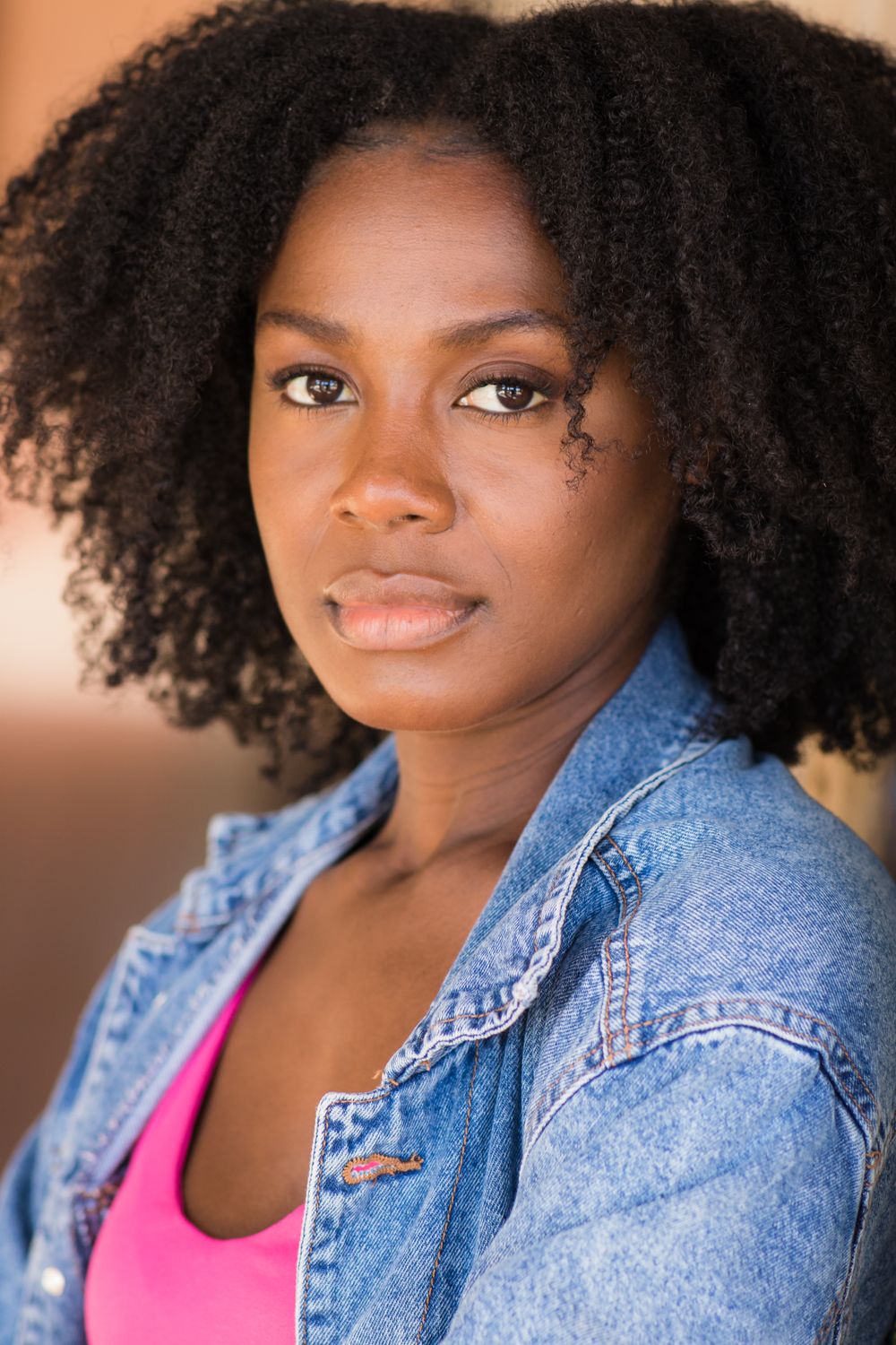 Portrait of woman with voluminous natural hair wearing denim jacket against warm background.