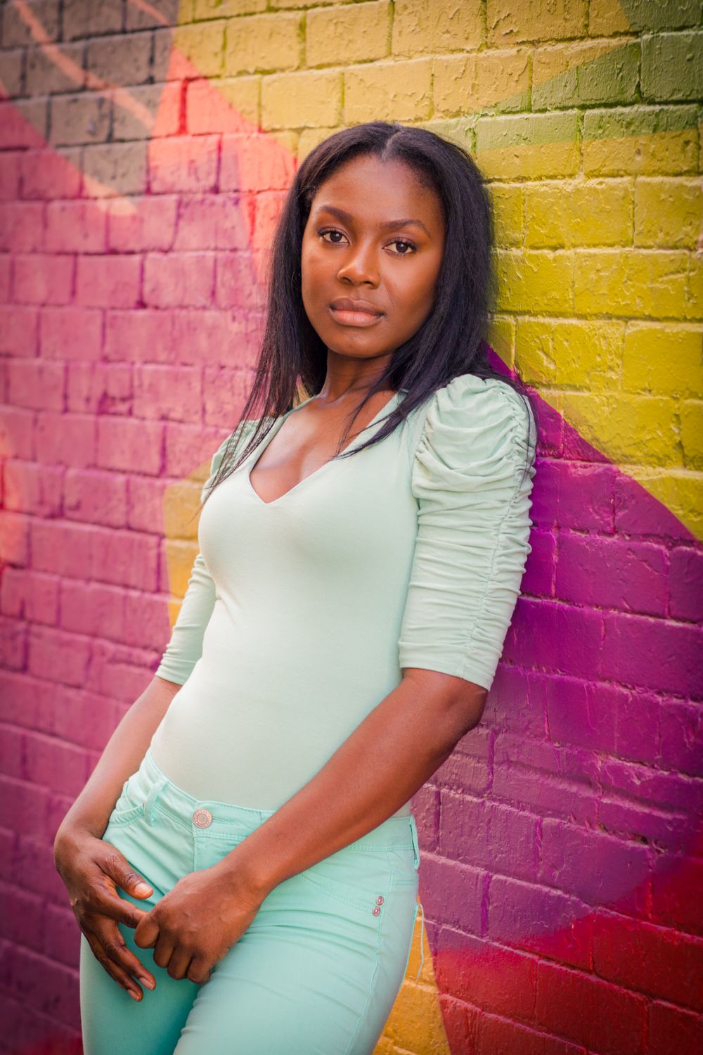 Casual portrait against colorful painted brick wall wearing mint pants and white top.