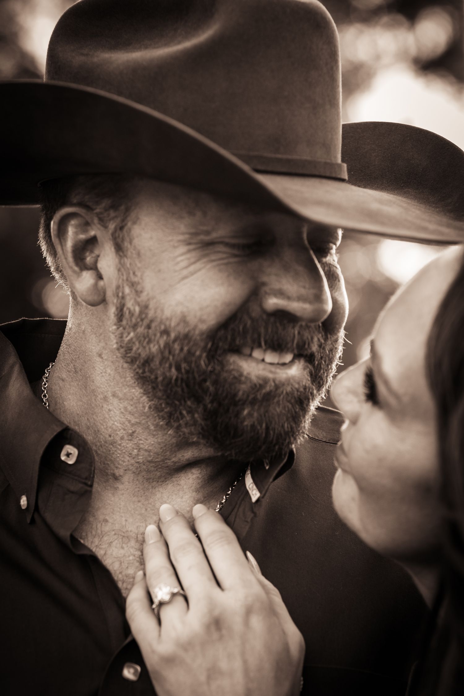 Sepia-toned intimate portrait of a couple sharing a romantic moment under a cowboy hat.