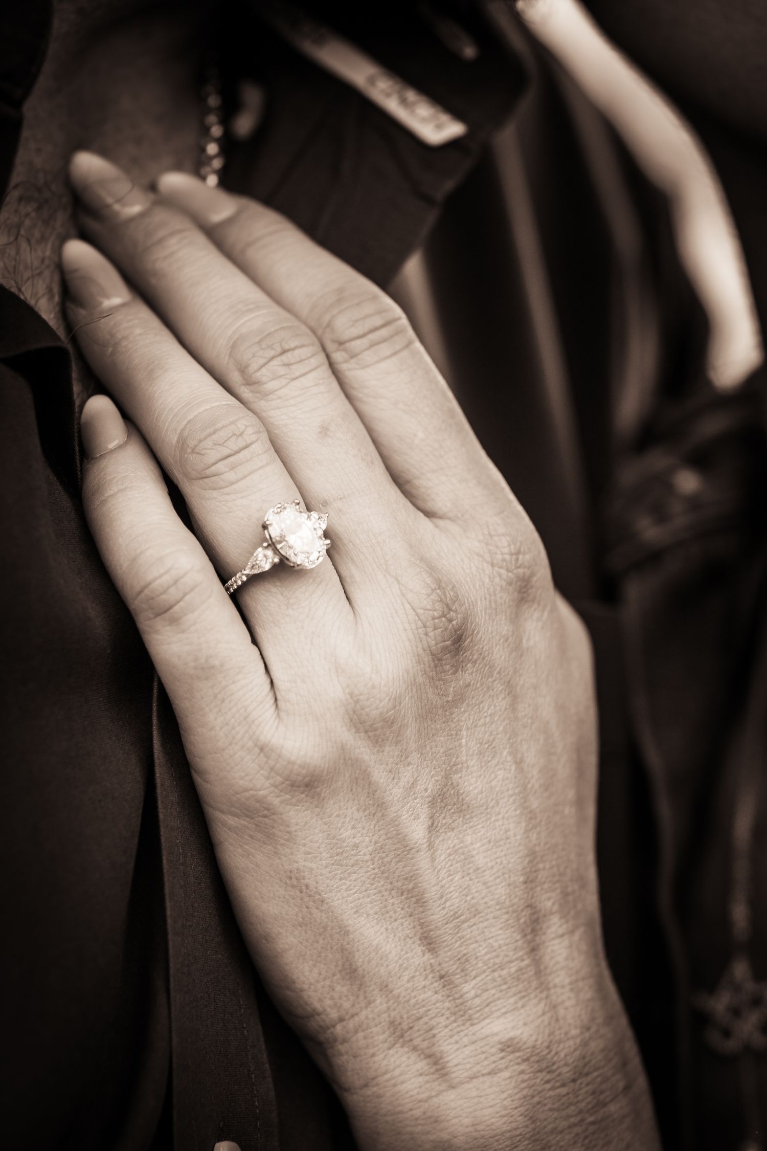 Black and white close-up of a delicate hand wearing an elegant engagement ring.