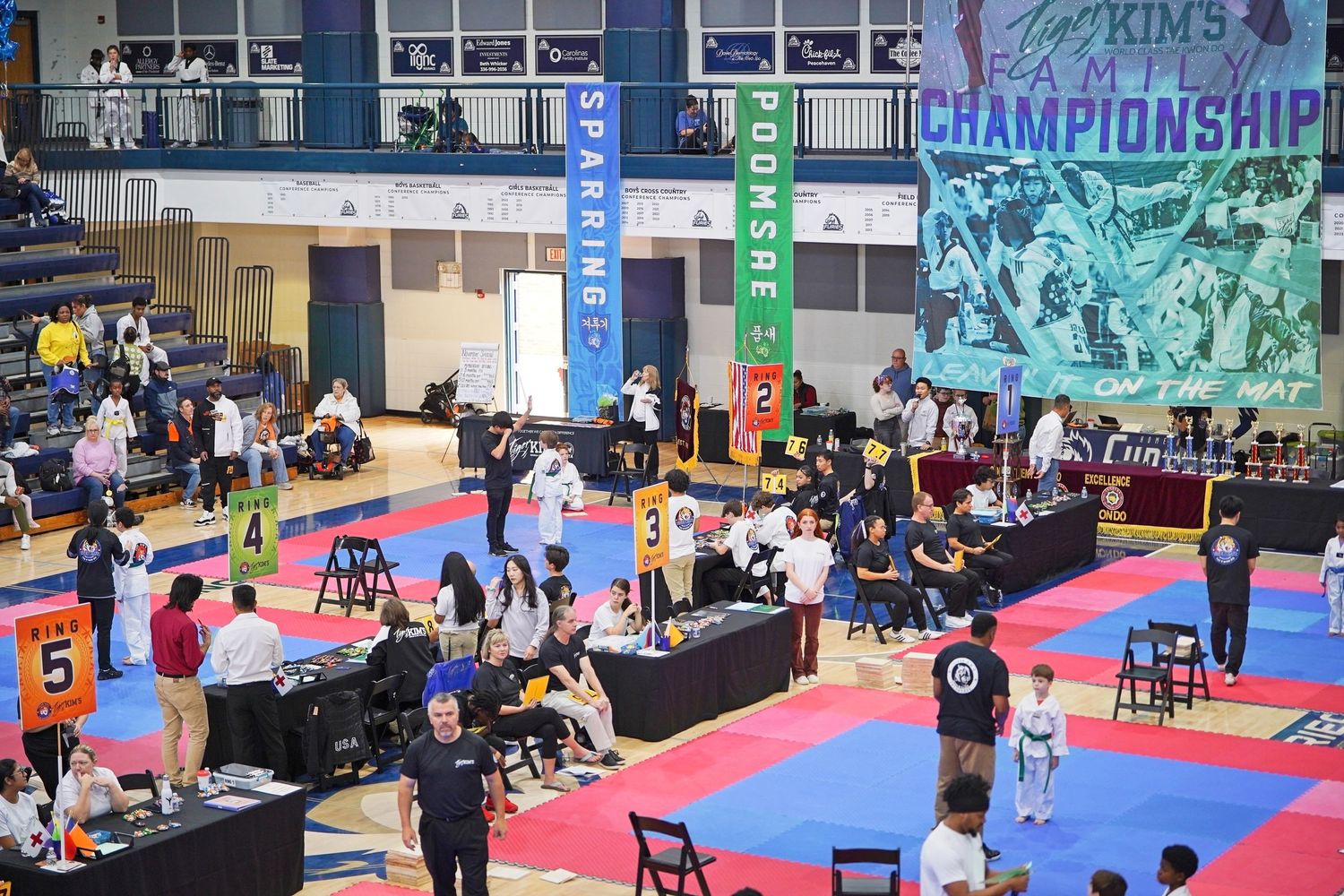 Indoor martial arts competition venue with multiple blue sparring mats and spectator seating.